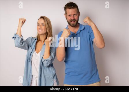 Ritratto di gente allegra uomo e donna in abbigliamento di base sorridente e clenching pugni come vincitori o persone felici isolato su sfondo bianco Foto Stock