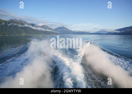 Traccia di onde da una barca galleggiante con un paesaggio di montagne meravigliose Foto Stock