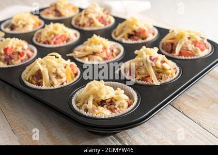 Muffin a base di lievito preparati con pomodori, verdure e formaggio in una teglia da forno pronta per il forno, fuoco selezionato, stretta profondità di fiel Foto Stock