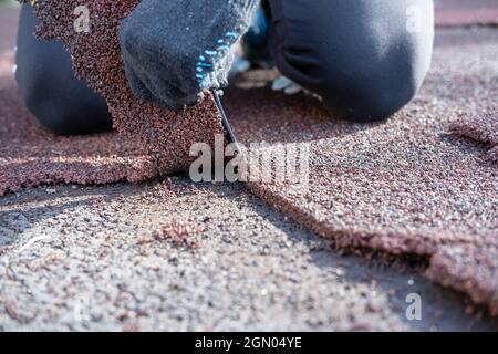 Le mani con guanti maschi riparano un terreno sportivo, tagliano con un coltello e rimuovono l'area danneggiata della copertura speciale. Foto Stock