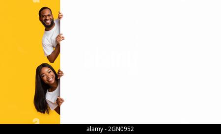 Coppia nera che sbirciava il cartellone pubblicitario bianco in studio Foto Stock