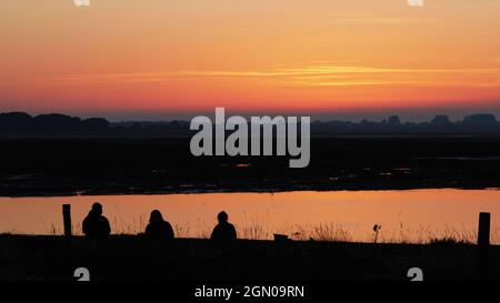 Tre persone hanno visto guardare il tramonto a Pagham, Regno Unito. Foto Stock