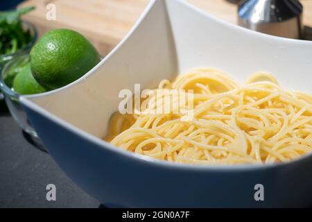 Spaghetti cotti in un recipiente bianco quadrato sul banco da cucina e pronti per la cottura Foto Stock