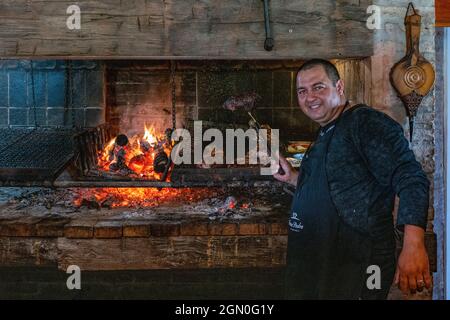 Il cuoco amichevole prepara la carne di asado deliziosa su griglia del carbone in Finca Piedra, San José de Mayo, Dipartimento di Colonia, Uruguay, Sudamerica Foto Stock