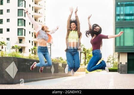Tre esuberante giovane donna felice che festeggia saltando in aria insieme ridendo e rallegrandosi in una strada della città Foto Stock
