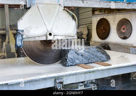 Taglio di un blocco di marmo italiano di Portoro nero in un laboratorio utilizzando una grande sega circolare a potenza raffreddata ad acqua in un primo piano sulla pietra sul lavoro Foto Stock