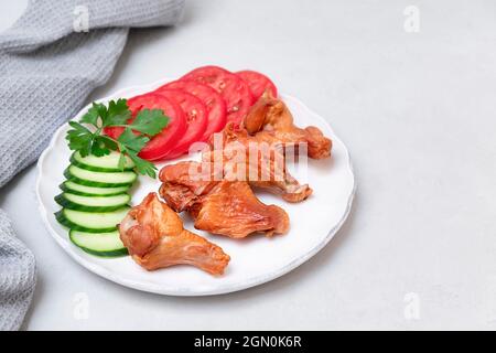 Ali di pollo affumicate su piatto bianco con insalata laterale su sfondo grigio neutro, spazio copia Foto Stock