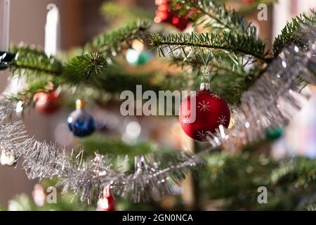 Primo piano di un ramo di albero di Natale con candele bianche, corona, tinsel colorati baubles al coperto durante il giorno. Classico verde, rosso Natale colori. SEL Foto Stock
