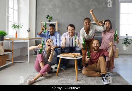 Gruppo di amici multirazziali maschi e femmine che guardano emotivamente una partita di calcio in TV a casa. Foto Stock