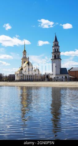 Torre pendente di Nevyansk e la chiesa dei credenti antichi (cupola) in primavera sulla riva del laghetto in Sverdlovsk Oblast, Russia. Scatto verticale. Foto Stock