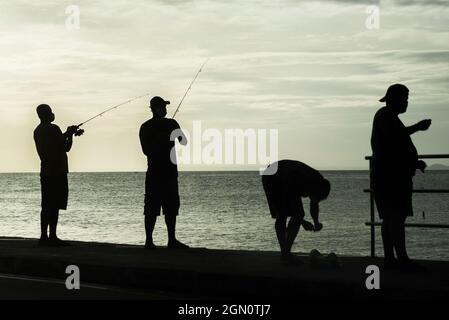 Salvador, Bahia, Brasile - 11 aprile 2021: Silhouette di pescatori con i loro pali al tramonto. Foto Stock