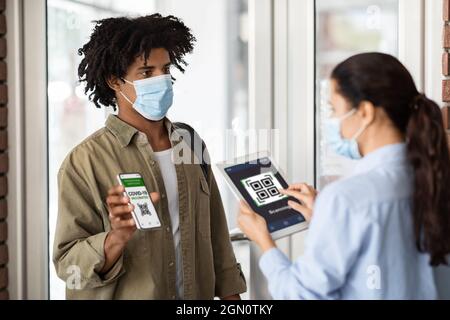 Giovane uomo Africano Americano che mostra certificato di vaccinazione su smartphone all'ingresso del Cafe Foto Stock