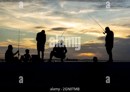 Salvador, Bahia, Brasile - 11 aprile 2021: Silhouette di pescatori con i loro pali al tramonto. Foto Stock
