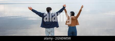 Vista posteriore della coppia che tiene le mani vicino al mare, banner Foto Stock