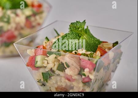 Insalata di macro tabouleh con prezzemolo, menta, bulgur, pomodori in tazza trasparente a buffet su sfondo bianco. Messa a fuoco selettiva Foto Stock
