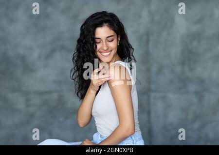 Giovane donna caucasica che mostra bendaggio adesivo sul suo braccio, ottenendo vaccinato contro il covid-19 su sfondo grigio Foto Stock