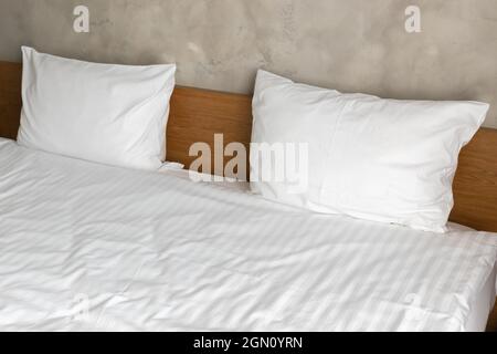 Due cuscini bianchi sono su un ampio letto vuoto con testiera in legno, astratto frammento interno della camera da letto Foto Stock