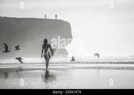 Surfista donna cammina sulla spiaggia in Portogallo con la sua tavola da surf, surf, Portogallo Foto Stock