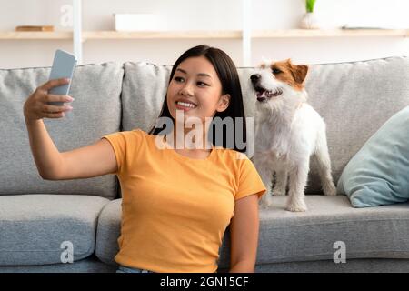 Sorridendo giovane donna asiatica che prende selfie con il suo cane carino Foto Stock