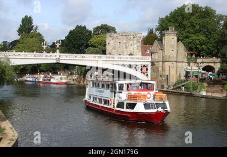 Vista dalla riva del fiume Ouse nel centro di York guardando verso il fiume in direzione del ponte Lendal con la barca da crociera della città, Captain James Cook, sull'acqua. Foto Stock