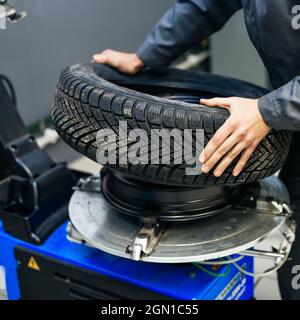 Immagine delle mani dei meccanici auto che mettono il pneumatico della vettura su cr in officina. Foto Stock