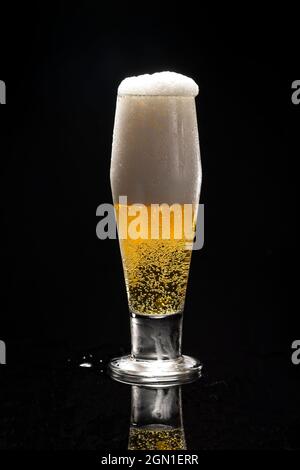 Un primo piano di un bicchiere di birra contro uno sfondo nero che inizia a traboccare. Foto Stock