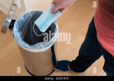 Un uomo che getta una maschera chirurgica blu usa e getta via in un bidone del pedale. Concetto: Anti masker, senza maschera facciale, maschera di binning, discussione maschera Foto Stock