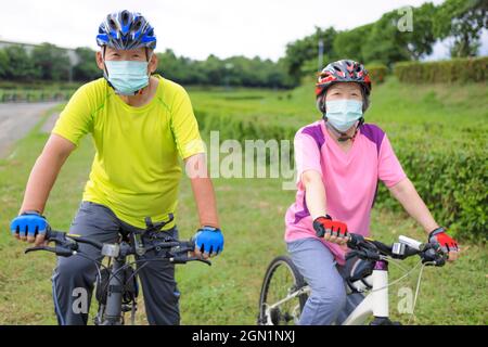 Asian Senior coppia indossare maschera medica e bicicletta a cavallo nel parco Foto Stock