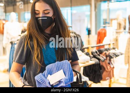 giovane donna latina che fa shopping in una boutique che guarda un maglione Foto Stock