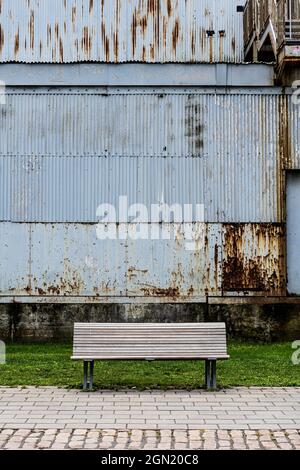 Scenario tranquillo di una panca vuota di fronte ad un vecchio edificio industriale Foto Stock