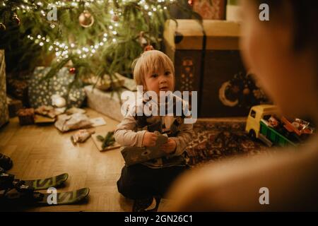 Il ragazzino svetta i suoi regali davanti all'albero di Natale, Natale, famiglia Foto Stock