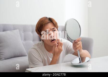 Giovane bell'uomo asiatico che guarda il suo volto nello specchio isolato Foto Stock