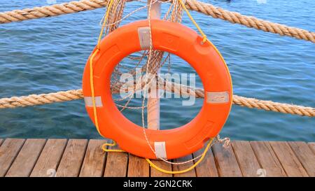 Linea di salvezza arancione e corde di mare sullo sfondo del mare e cielo blu. Funi marine e salvagente appesi su un palo. Concetto di aiuto e sicurezza Foto Stock