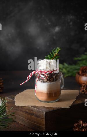 Regalo di Natale commestibile fatto in casa in vasetto di mason per una bevanda al cioccolato su sfondo scuro. Primo piano. Delizie natalizie. Formato verticale. Foto Stock