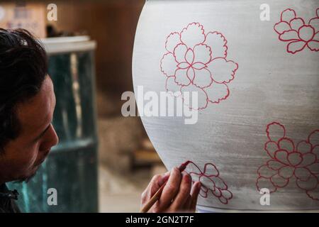 Cibuntu, Indonesia, 22/09/2021, Un artigiano disegna un fiore su un vaso di ceramica in Mekarbakti Village.vasi di ceramica da qui sono stati venduti a varie regioni in Indonesia come l'isola di Bali e sono stati venduti a paesi stranieri come gli Stati Uniti e l'Africa. I prodotti ceramici dall'Indonesia hanno varie forme che variano da caraffe di ceramica, decorazioni a forma di pesce, grandi vasi, statue di ceramica, piatti, bicchieri, a pagode. La gamma di prezzi dipende dalla dimensione e dal livello di complessità; il prezzo per un metro di vaso di ceramica alto è IDR 900,000 ($63.00). Foto Stock