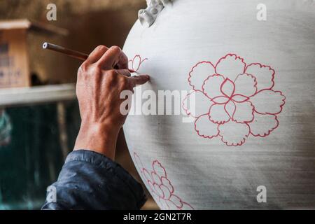 Cibuntu, Indonesia, 22/09/2021, Un artigiano disegna un fiore su un vaso di ceramica in Mekarbakti Village.vasi di ceramica da qui sono stati venduti a varie regioni in Indonesia come l'isola di Bali e sono stati venduti a paesi stranieri come gli Stati Uniti e l'Africa. I prodotti ceramici dall'Indonesia hanno varie forme che variano da caraffe di ceramica, decorazioni a forma di pesce, grandi vasi, statue di ceramica, piatti, bicchieri, a pagode. La gamma di prezzi dipende dalla dimensione e dal livello di complessità; il prezzo per un metro di vaso di ceramica alto è IDR 900,000 ($63.00). Foto Stock