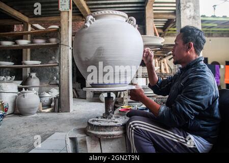 Cibuntu, Indonesia, 22/09/2021, Un artigiano disegna un fiore su un vaso di ceramica in Mekarbakti Village.vasi di ceramica da qui sono stati venduti a varie regioni in Indonesia come l'isola di Bali e sono stati venduti a paesi stranieri come gli Stati Uniti e l'Africa. I prodotti ceramici dall'Indonesia hanno varie forme che variano da caraffe di ceramica, decorazioni a forma di pesce, grandi vasi, statue di ceramica, piatti, bicchieri, a pagode. La gamma di prezzi dipende dalla dimensione e dal livello di complessità; il prezzo per un metro di vaso di ceramica alto è IDR 900,000 ($63.00). Foto Stock