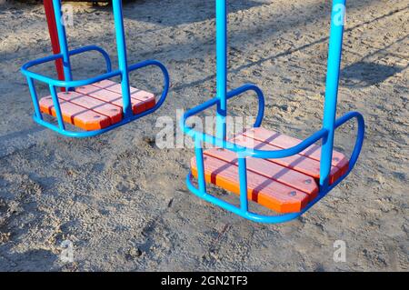 Altalene colorate in metallo con posto a sedere in legno sul parco giochi per bambini Foto Stock