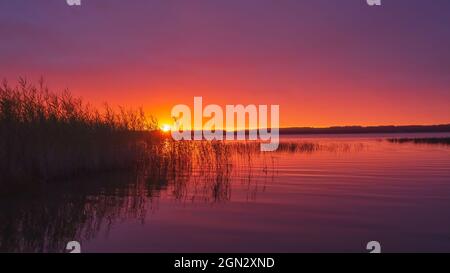 Tramonto rosso sul lago con riflessi nell'acqua Foto Stock