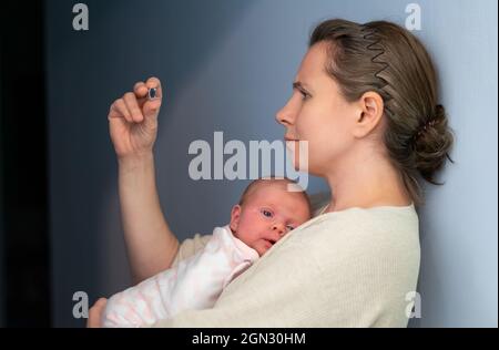 Madre preoccupata che guarda il termometro che tiene il suo neonato nelle mani. Foto Stock