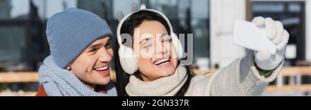 donna felice in maglione e cuffie cuffie con selfie con ragazzo in inverno, banner Foto Stock