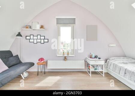 Design creativo della camera da letto per bambini con finestra tra divano e letto su parquet a casa in luce solare Foto Stock