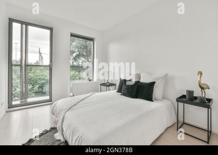 Interno di spaziosa camera da letto luminosa con comodo letto e grandi finestre in appartamento moderno di giorno Foto Stock