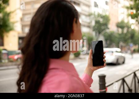 Ritagliare anonima femmina in piedi sul marciapiede e scattare foto sul telefono cellulare in città Foto Stock
