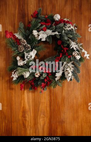 Elegante corona di Natale con rametti di conifere ed elementi decorativi appesi su pareti di legno alla luce del giorno Foto Stock