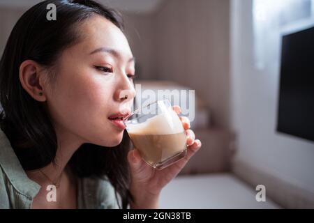Vista laterale di giovani donne etniche blogger alla scrivania bere caffè a casa Foto Stock