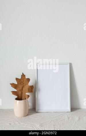 Casa decoratore moccap, quadro vuoto cornice vicino bianco dipinto muro di cemento, rami con foglie asciutte Foto Stock