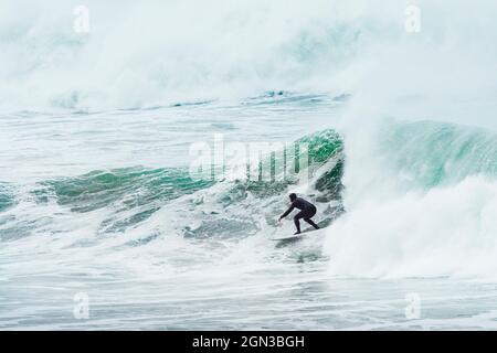 Un surfista che cavalcano enormi onde costruendo sopra la barriera corallina di Cribbar al largo della costa di Newquay in Cornwall.West Country; Inghilterra; Regno Unito; Europa Foto Stock