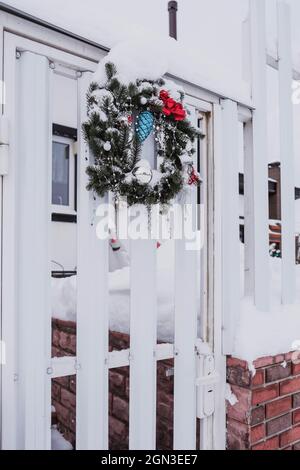 Corona di Natale decorata con palle e archi rossi sulle porte all'esterno coperte di neve Foto Stock