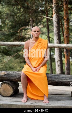 uomo a piedi nudi in accappatoio tradizionale buddista seduta su panca di legno nella foresta Foto Stock